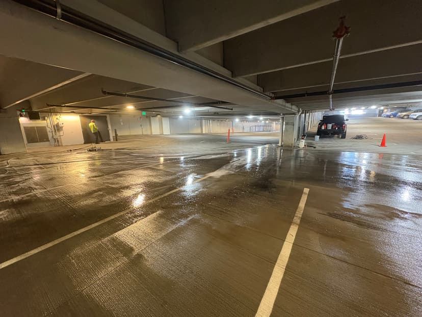 Clean parking garage with wet floors and maintenance worker visible in the background.