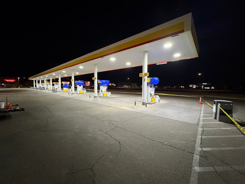 Deserted gas station at night with illuminated pumps and caution tape.