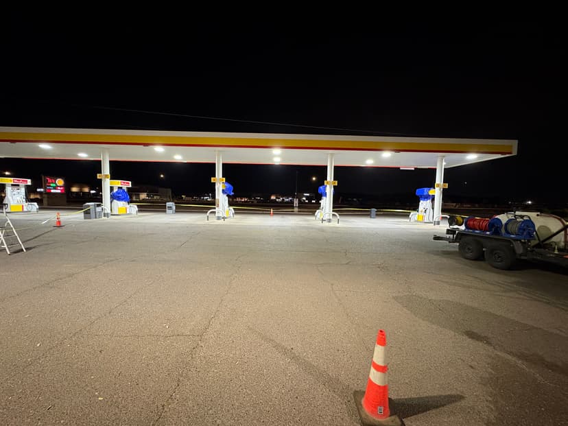 Gas station at night with illuminated pumps, marked cones, and a service trailer nearby.
