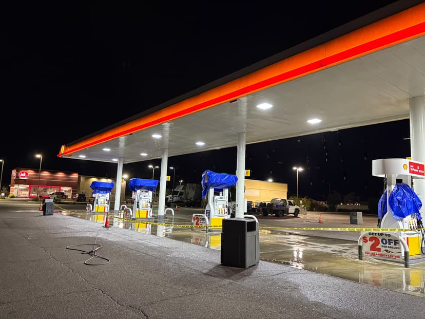 Night view of a gas station with covered pumps and illuminated signage, rain-soaked pavement.